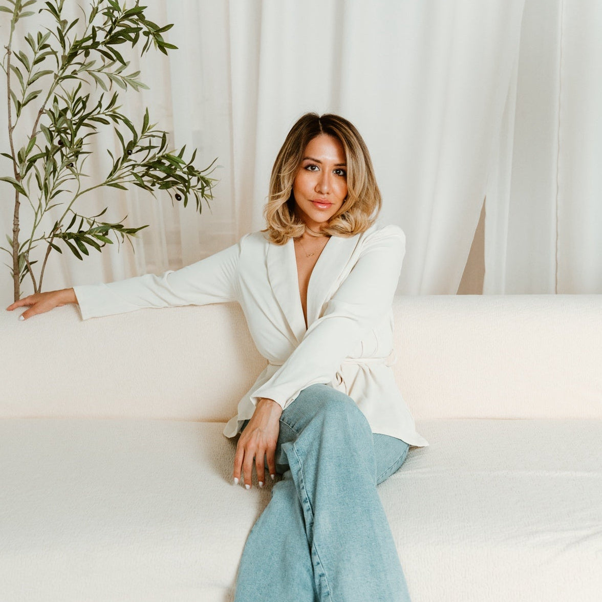 Woman sitting on a white couch holding a plant in a minimalistic setting